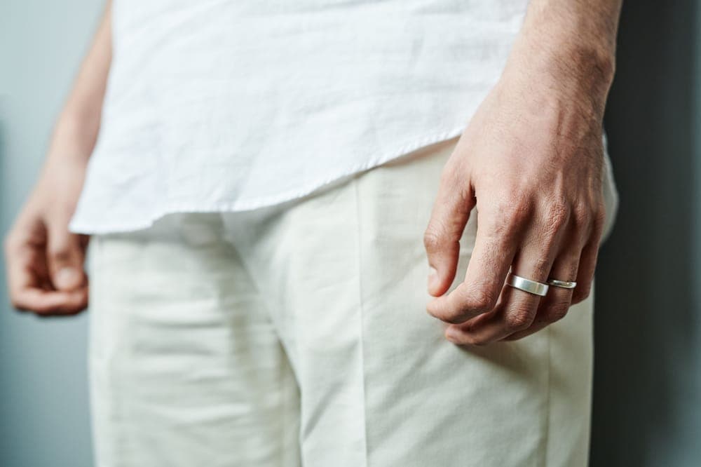 A man's hand wearing two silver bands against a white shirt