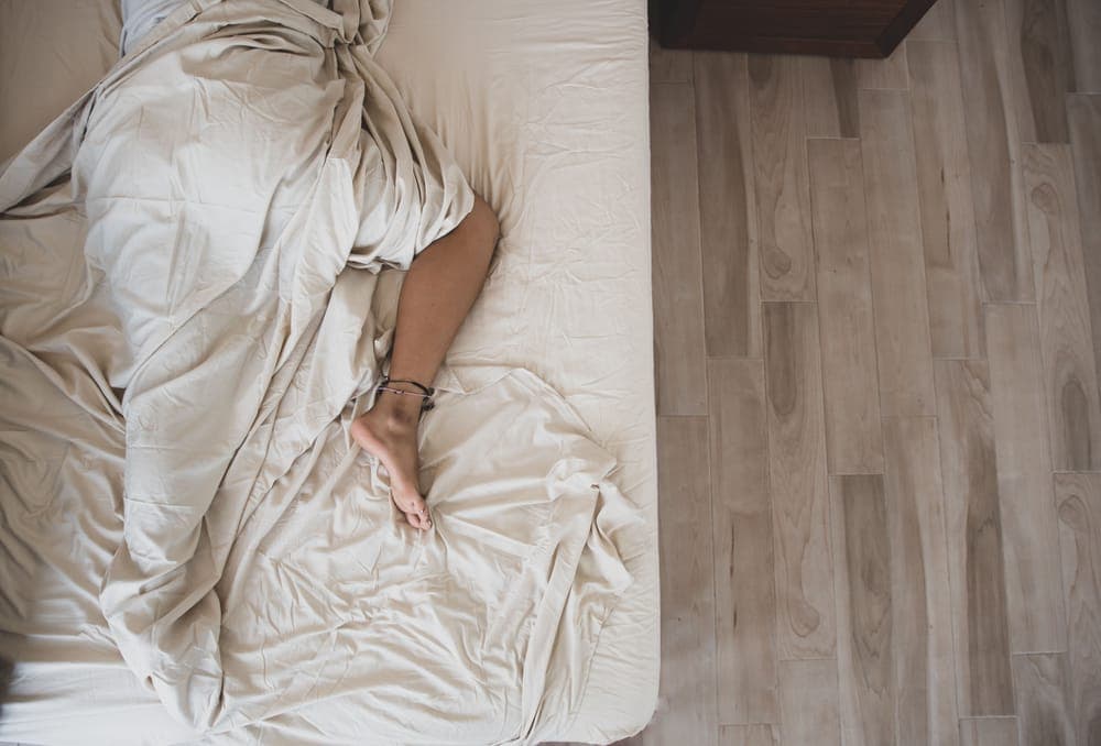 Overhead view of a person asleep under beige sheets
