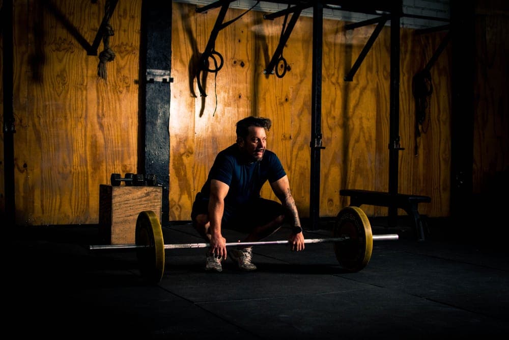 A man crouched over a loaded barbell in a dim gym