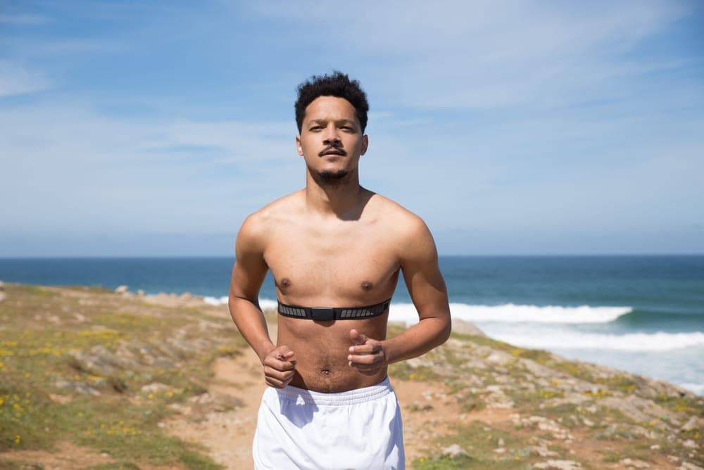 A man jogging on a coastal path wearing a black heart-rate chest strap