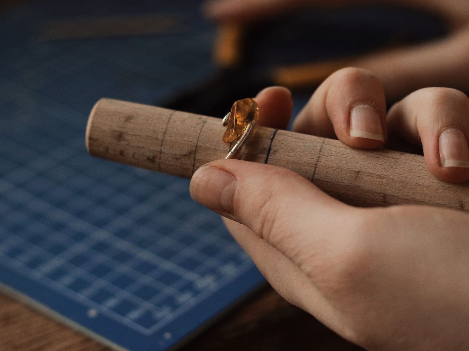 Hands holding a wooden ring mandrel with size lines and a ring on it
