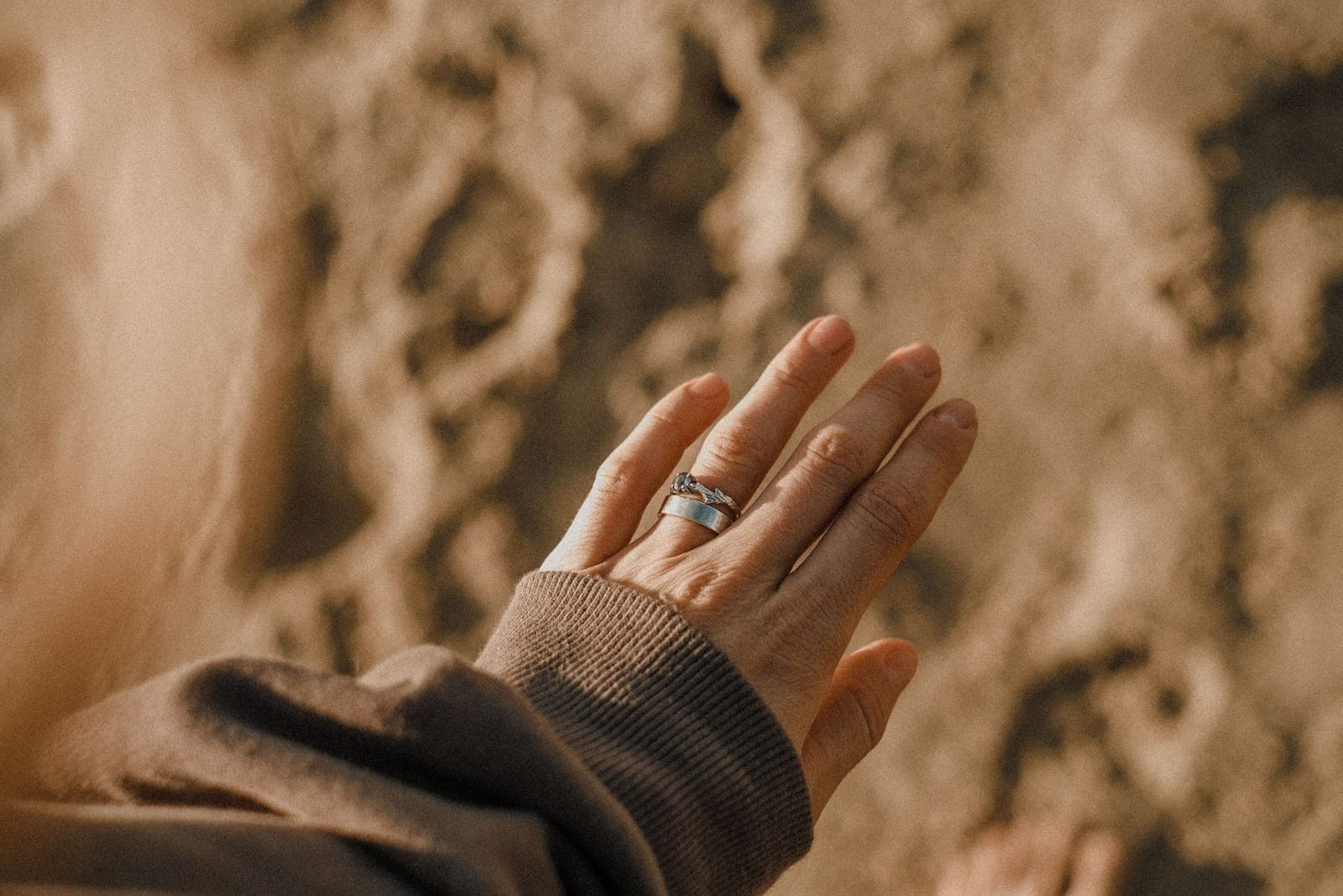 A hand wearing two silver rings on one finger in warm sunlight